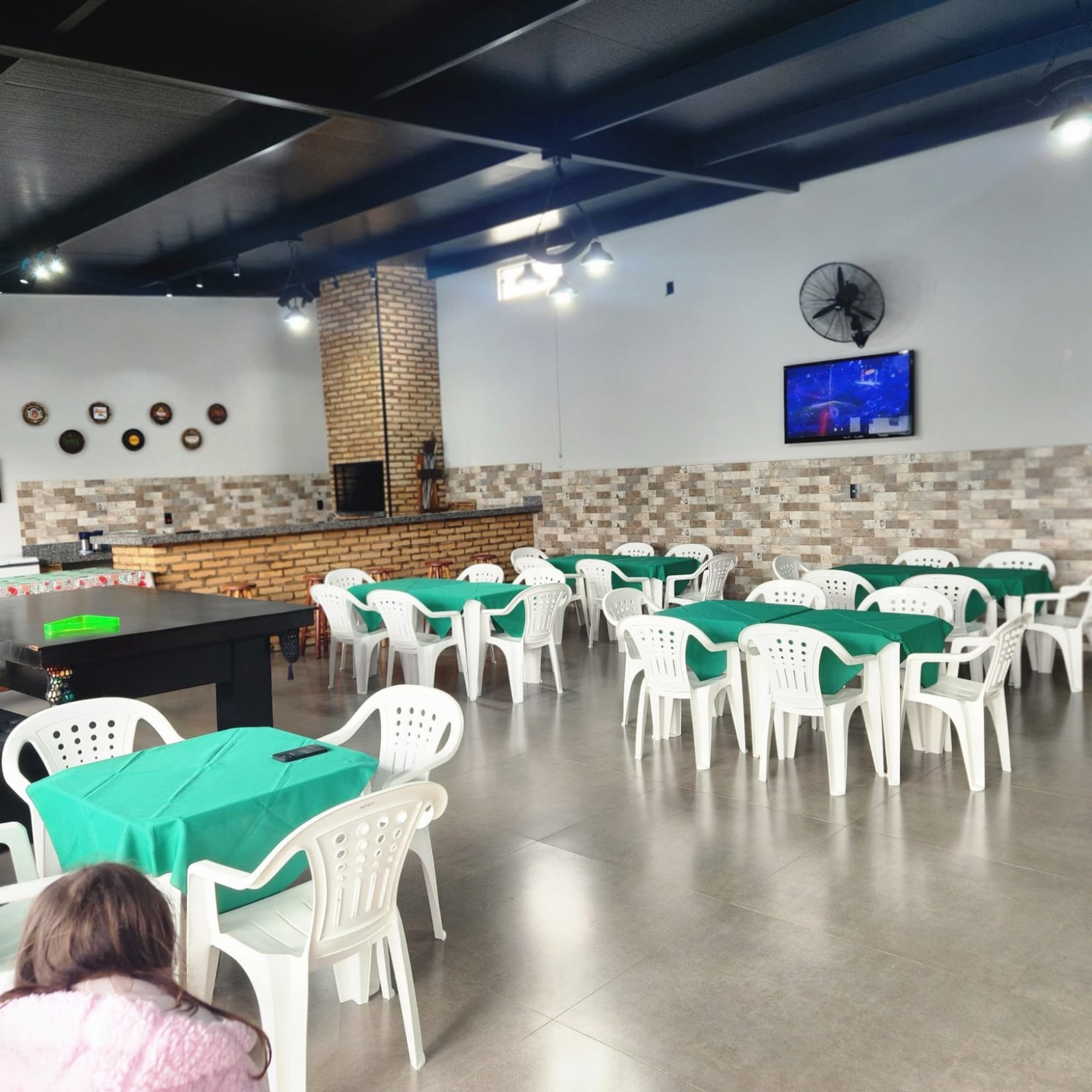 Mesas com toalha verde e cadeiras brancas no salão
